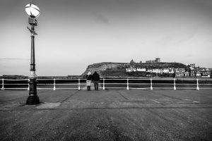 A-Couple-on-the-Pier-with-Whitby-Abbey-in-the-Distance-North-Yorkshire-Coast-England.