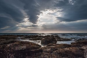 Shafts-of-sunlight-bursting-through-clouds-on-rocky-coastline-The-Catlins-New-Zealand